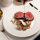 Sauce being poured over a plate of beef and mushrooms that is on a laid table